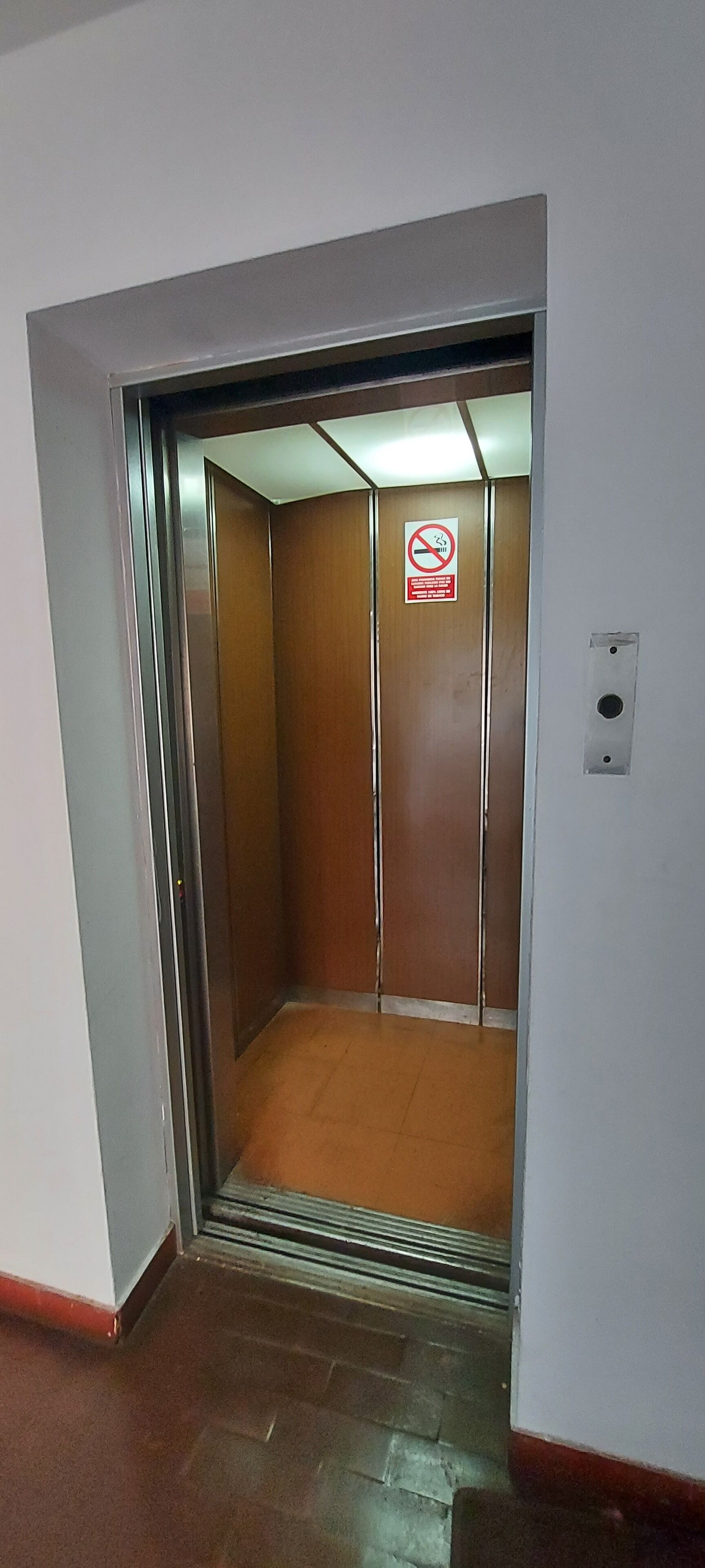 An elevator with a no-smoking sign, a wooden interior, and a metal door.