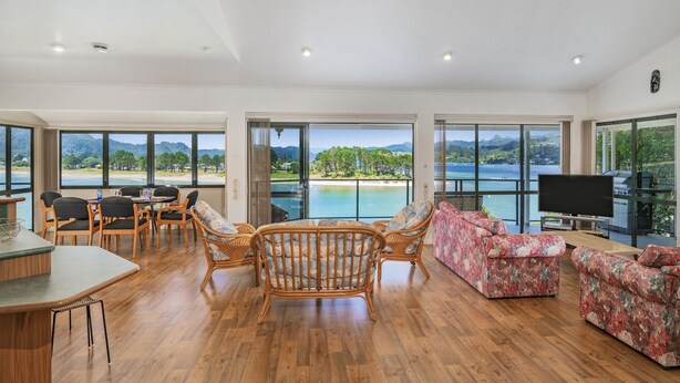 A spacious living area with a wooden floor, a dining set, and a large TV. - Pohutukawa on Paku - Tairua Holiday Home (Tairua)