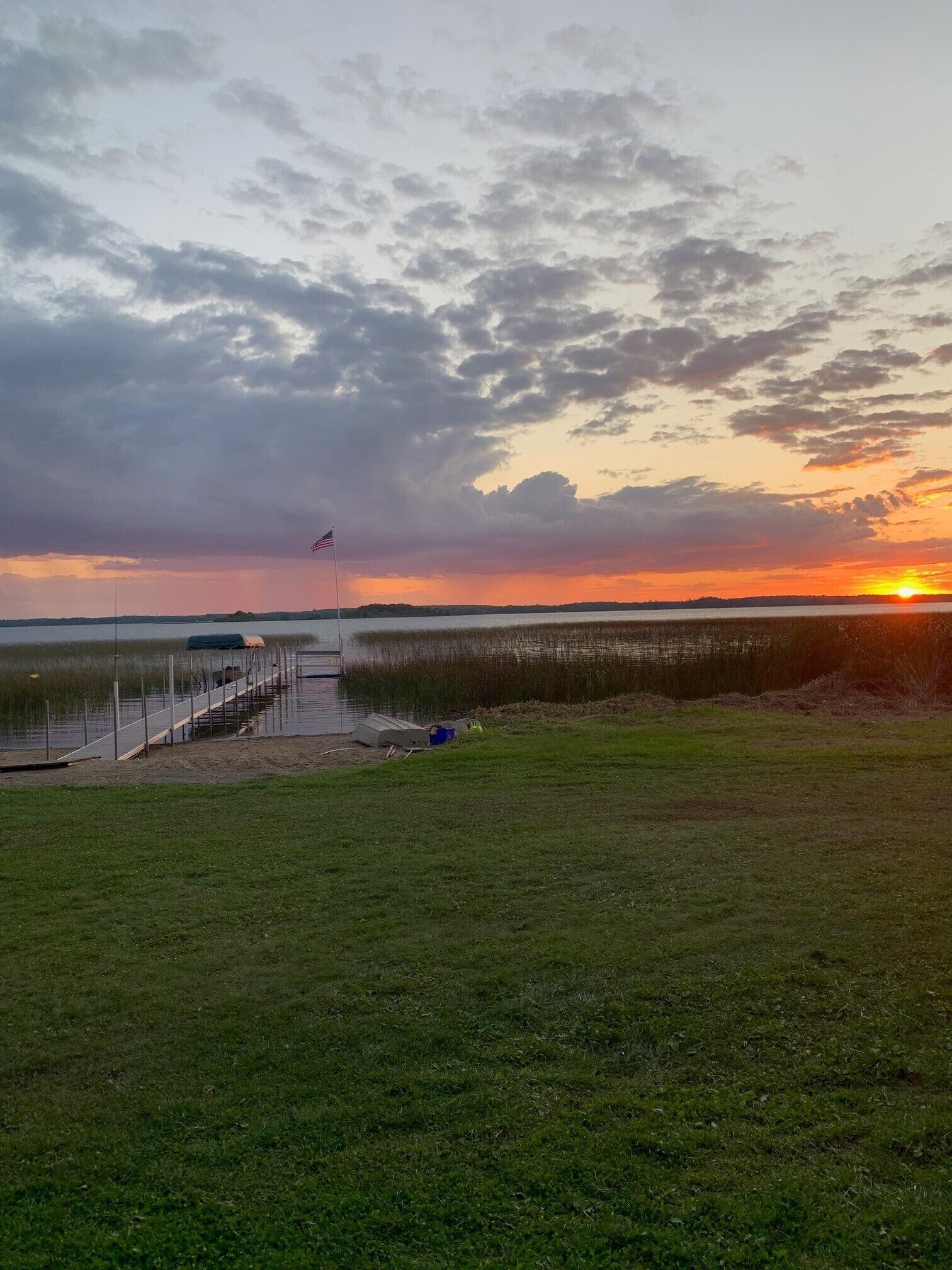 A sunset over a body of water with a dock and grassy area in the foreground.
