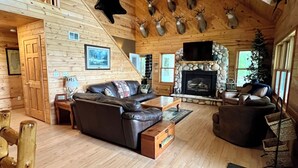 Un intérieur de chalet en bois spacieux, doté d’une cheminée, de sièges en cuir et de têtes d’animaux fixées au plafond.
