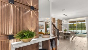 Une cuisine moderne avec un mur d’accent en bois, un plan de travail blanc et un coin repas offrant une vue sur l’extérieur.