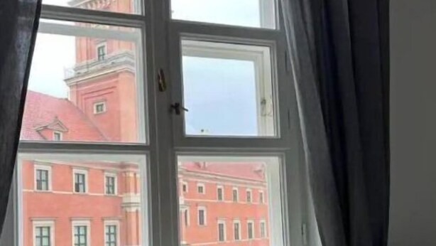 Une pièce avec une fenêtre donnant sur un bâtiment à la façade rouge et surmonté d’un dôme.