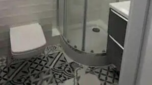 Une douche d’angle avec une porte en verre, un petit banc blanc et un sol carrelé.