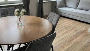 Un salon moderne avec une table de salle à manger ronde en bois, des chaises à revêtement gris, un canapé gris et une fenêtre avec des rideaux.