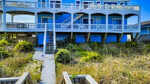 Ein mehrstöckiges Strandhaus mit einer Holzterrasse und einer Treppe zu den oberen Stockwerken.
