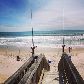A wooden boardwalk leading to a beach with two fishing rods set up.