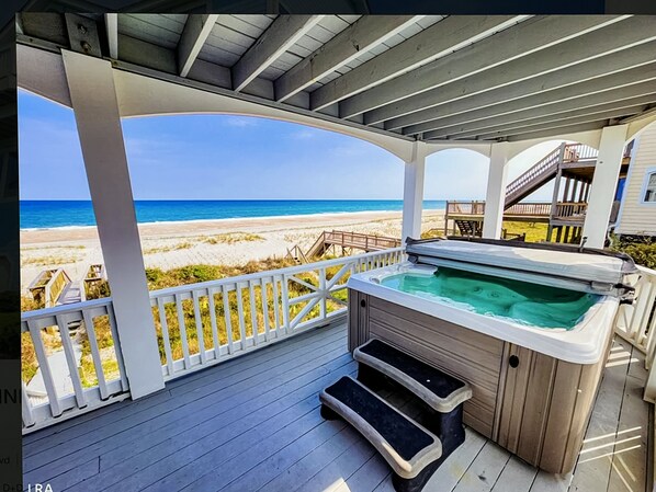 A covered deck with a hot tub, wooden steps, and a view of the beach.