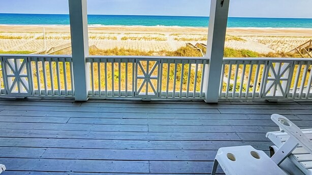 Eine Holzterrasse mit Blick auf Strand und Meer.