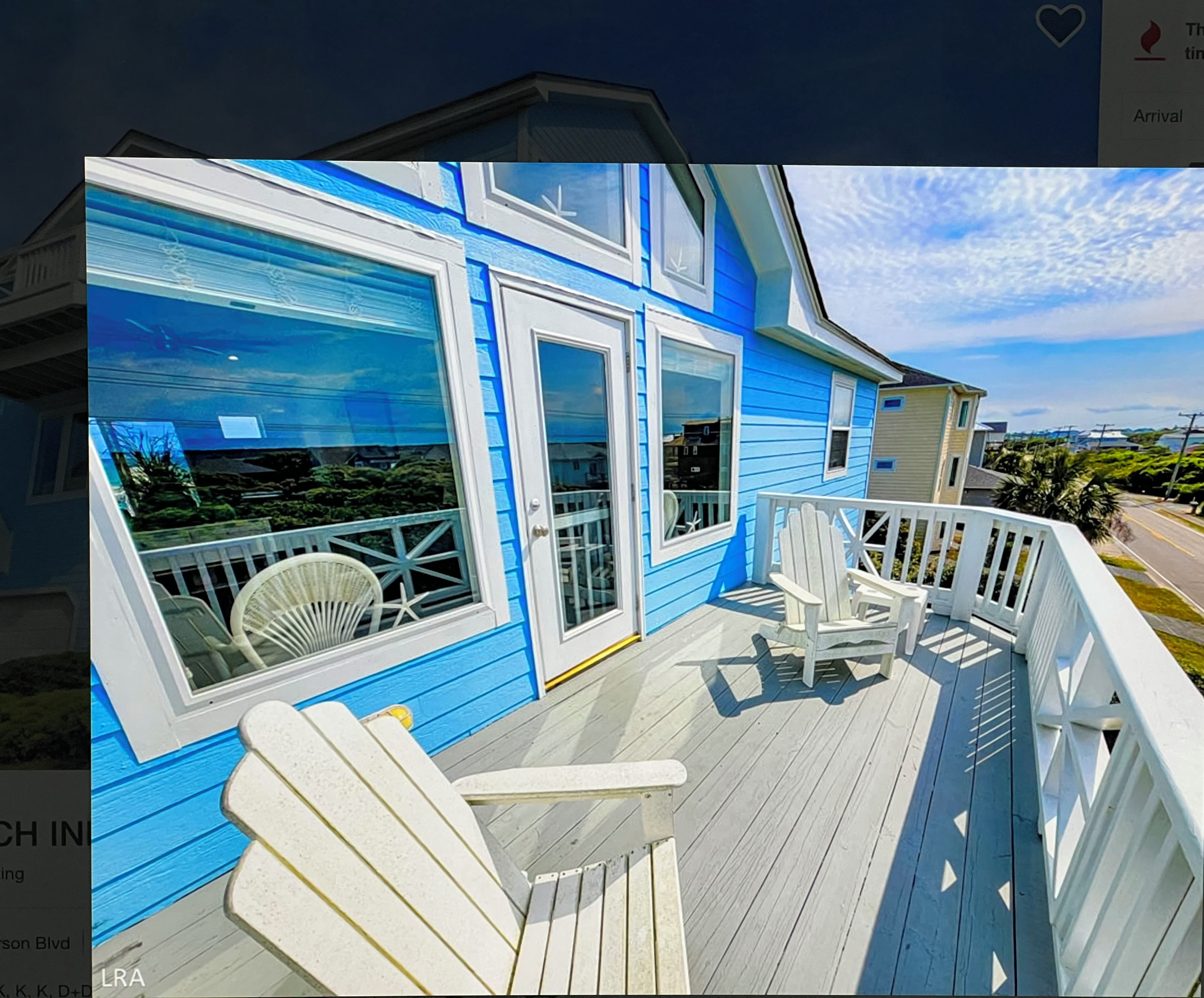A blue house with a wooden deck and white chairs.
