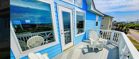A blue house with a wooden deck and white chairs.