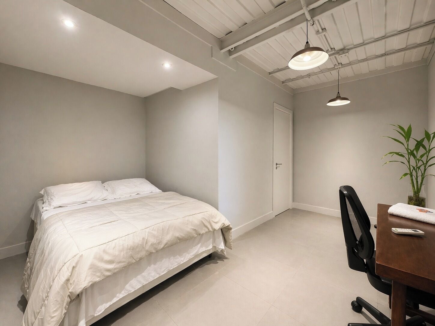 A bedroom with a bed, a desk, a chair, and a potted plant.
