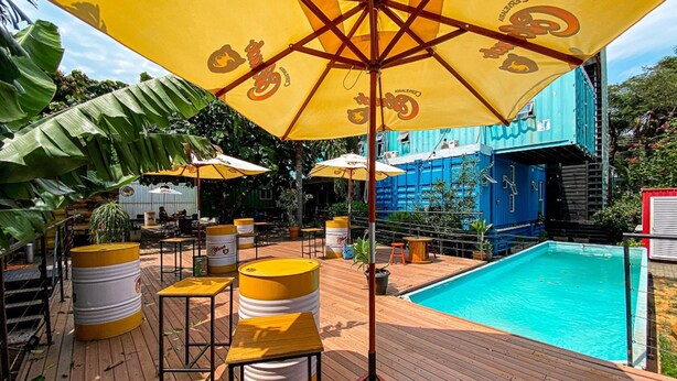 A poolside area with yellow umbrellas, wooden deck, and a pool. - Tetris Container Hostel (Foz do Iguaçu)