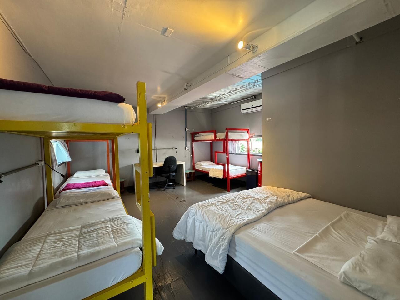 A dormitory room with bunk beds, a desk, and an air conditioning unit.