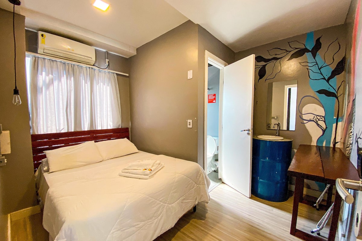 A hotel room with a bed, a bedside table, a mirror, a bathroom with a sink, and a toilet.