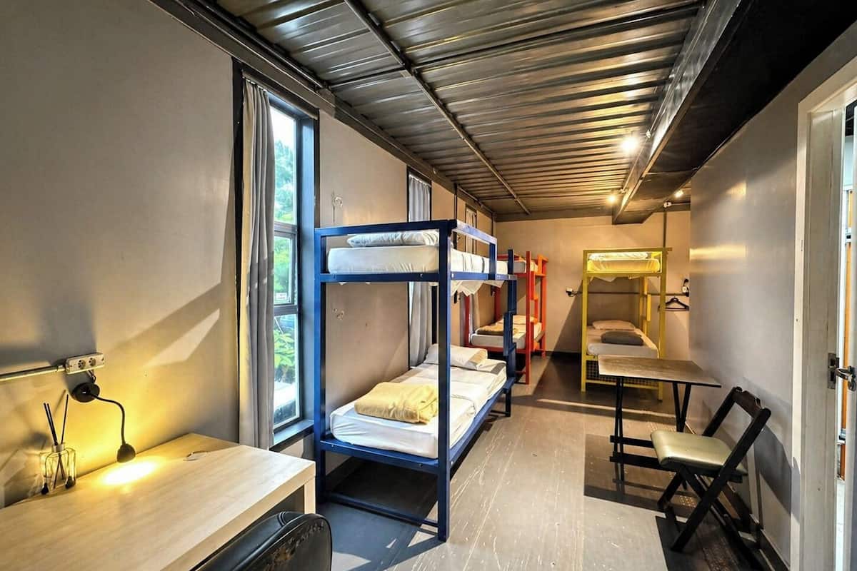 A dormitory room with bunk beds, a desk, a chair, and a window with curtains.