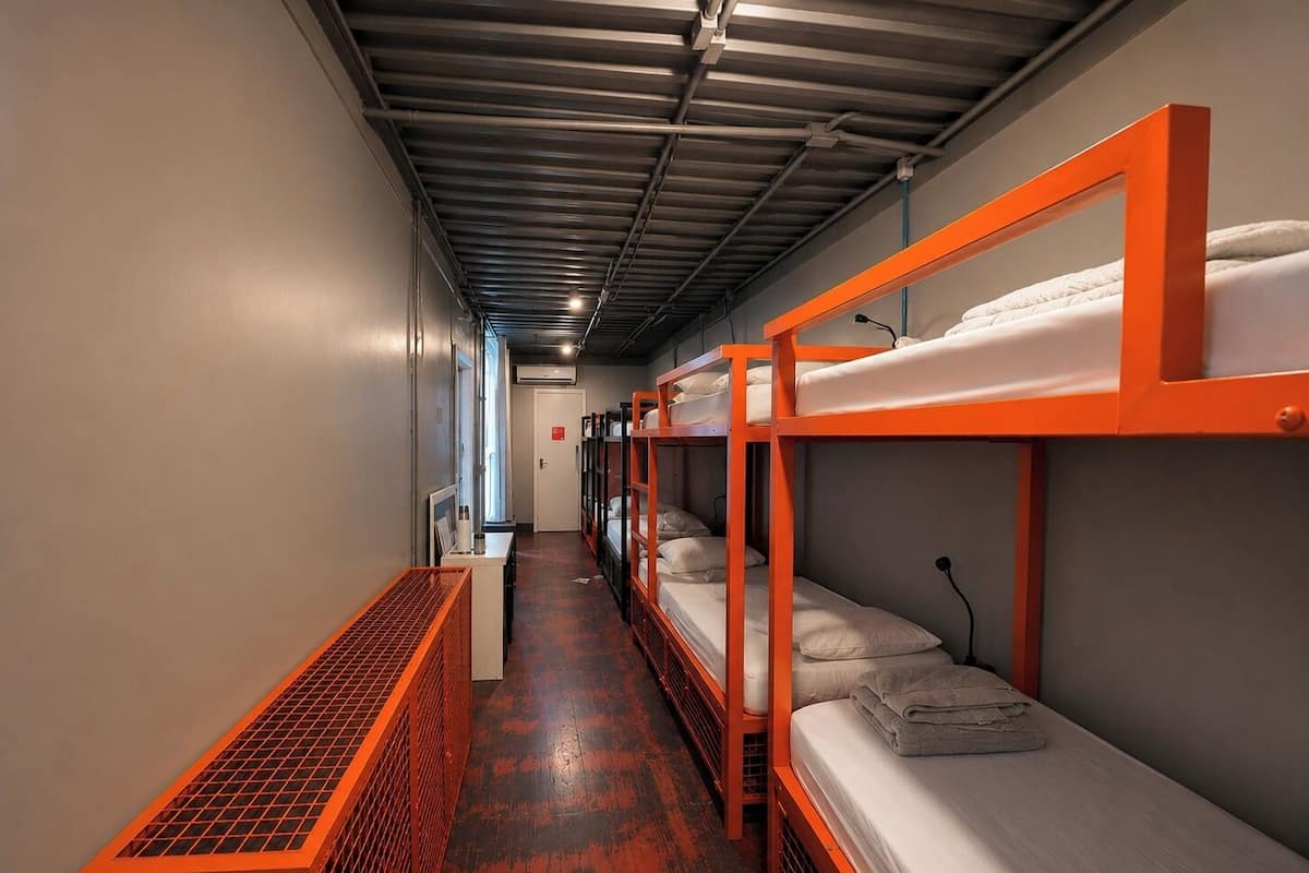 A narrow corridor with bunk beds and a bench, leading to a door at the end.