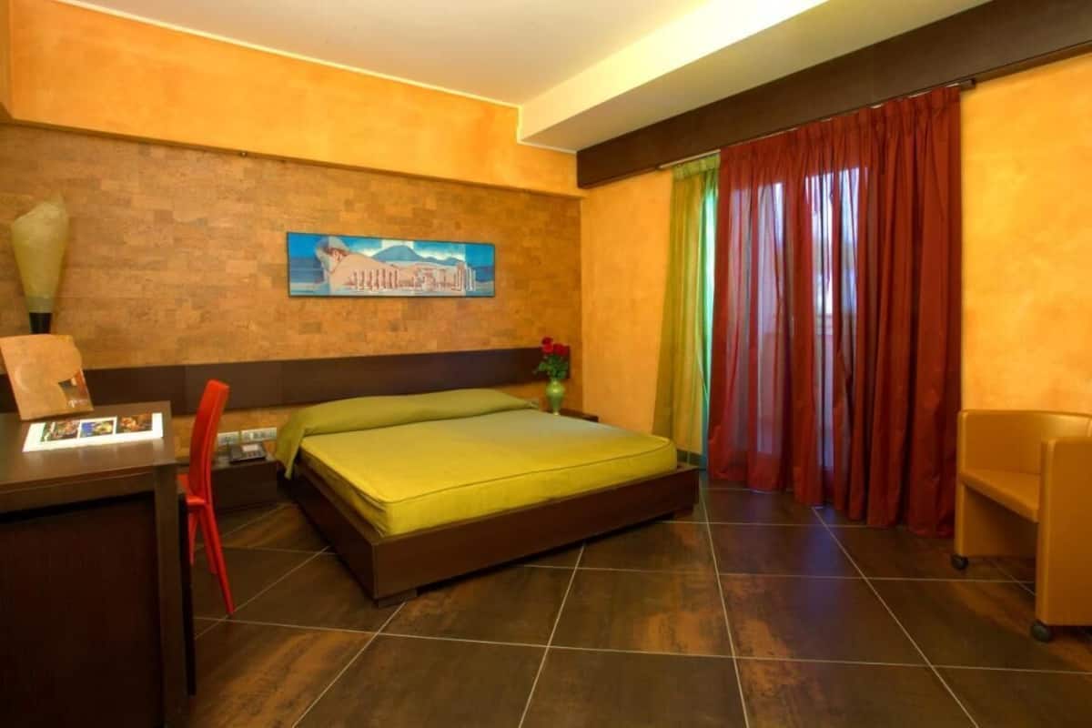 A hotel room with a bed, a desk, a chair, and a large window with curtains.