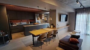 Una cocina moderna con una isla central, comedor con sillas, un sofá y un televisor montado en la pared.