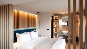 Habitación de hotel moderna con una cama grande, cabecera de madera y tocador integrado con espejo y lavabo.