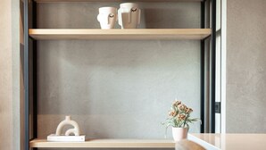 Un interior moderno con una estantería minimalista, una planta en maceta y un otoman tejido a rayas.