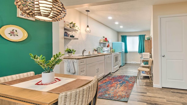 Une cuisine moderne avec des meubles blancs, une table à manger en bois et un tapis aux couleurs vives.