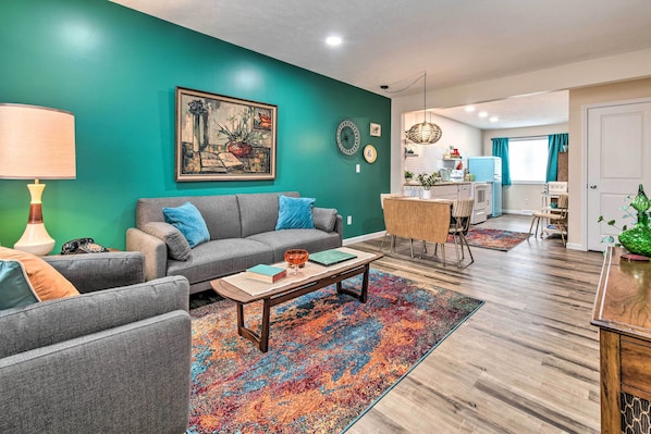 Una sala de estar con una pared verde azulado, un sofá gris, una mesa de centro y una alfombra colorida.