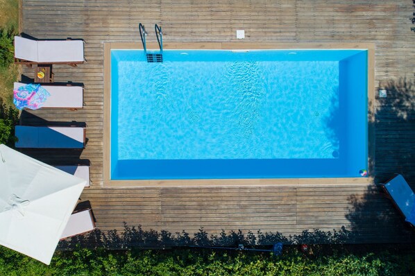 A rectangular swimming pool with a wooden deck, lounge chairs, and a ladder.