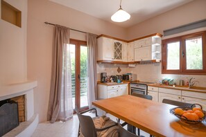 A kitchen with a wooden table, a fireplace, and a window with curtains.