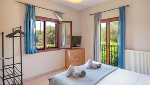 A bedroom with a bed, a TV on a wooden dresser, a drying rack, and a balcony with curtains. - Jennys House in Stroggili (Corfu)