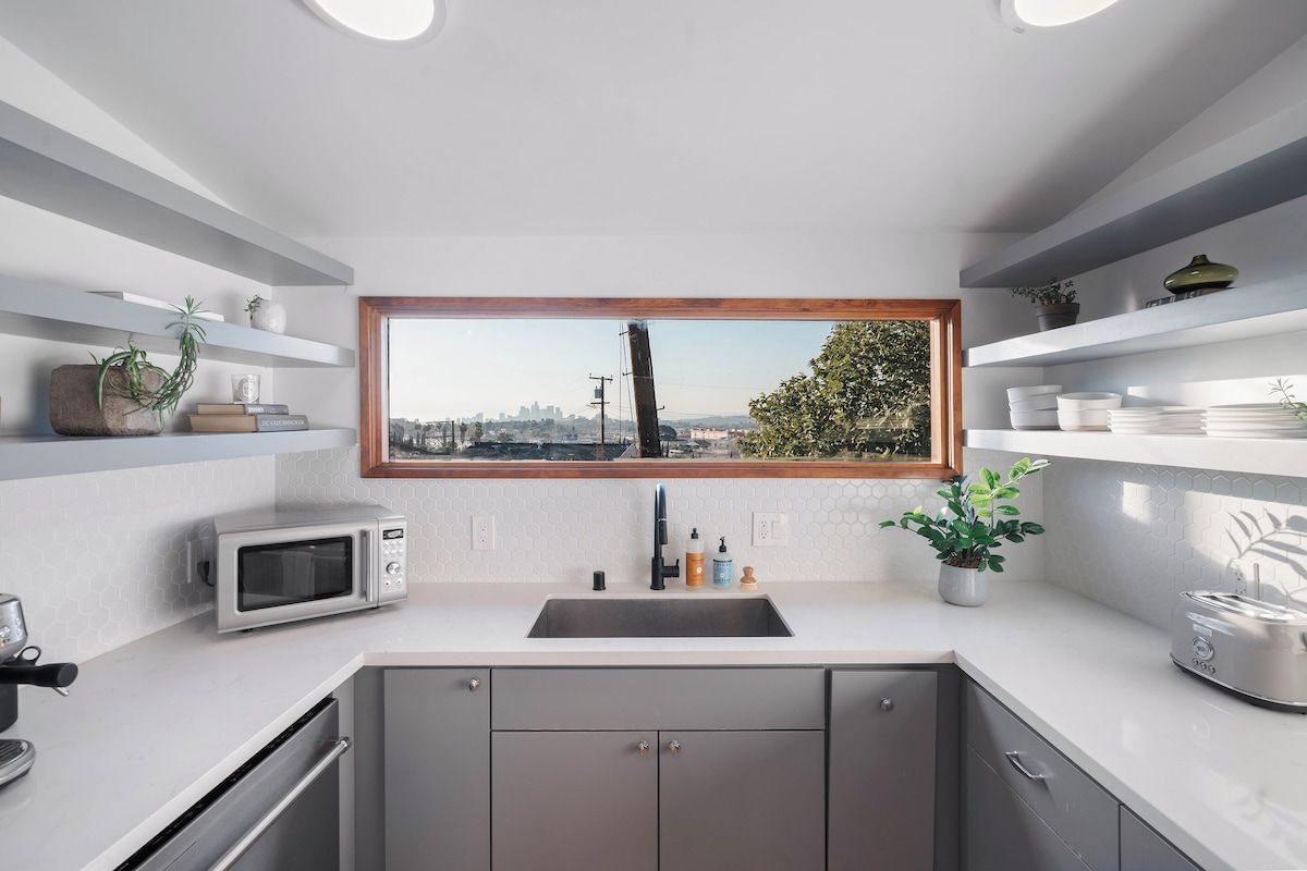 Une cuisine moderne équipée d’un four à micro-ondes encastré, d’un évier et d’une fenêtre donnant sur la ville.