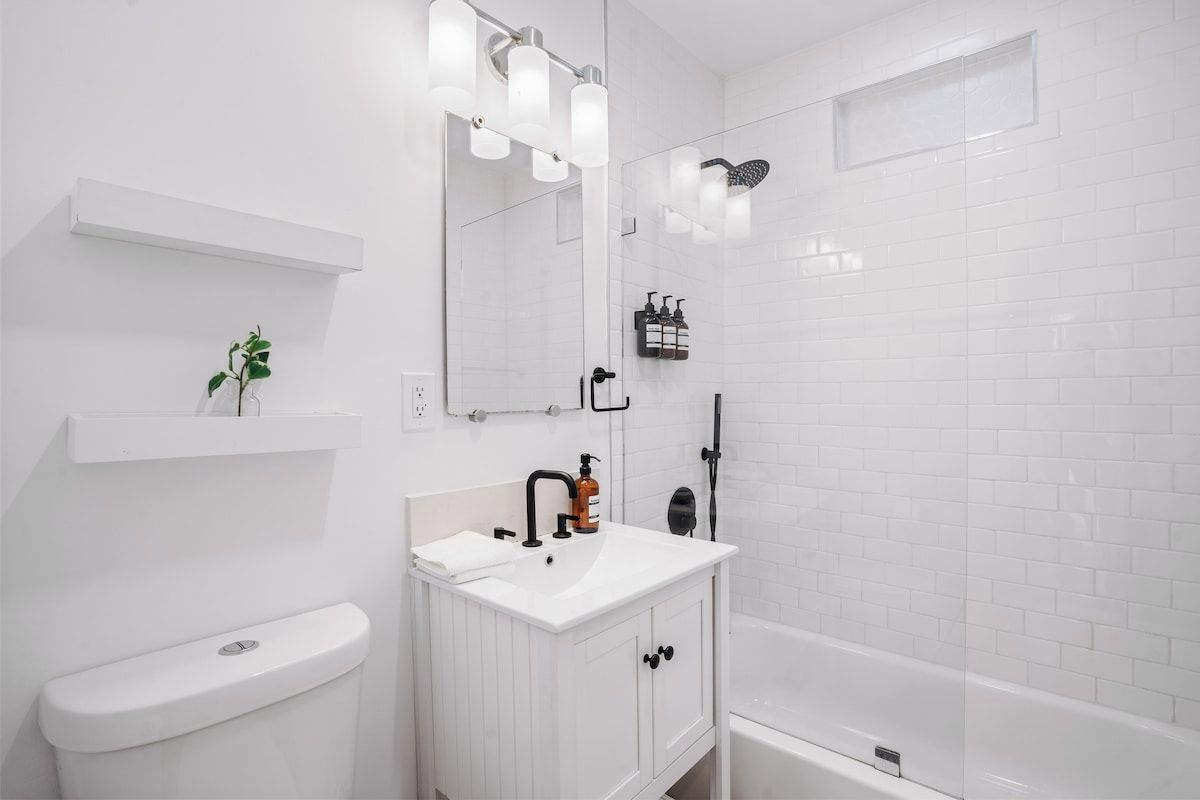 Et hvidt badeværelse med toilet, håndvask med spejl og bruseområde.