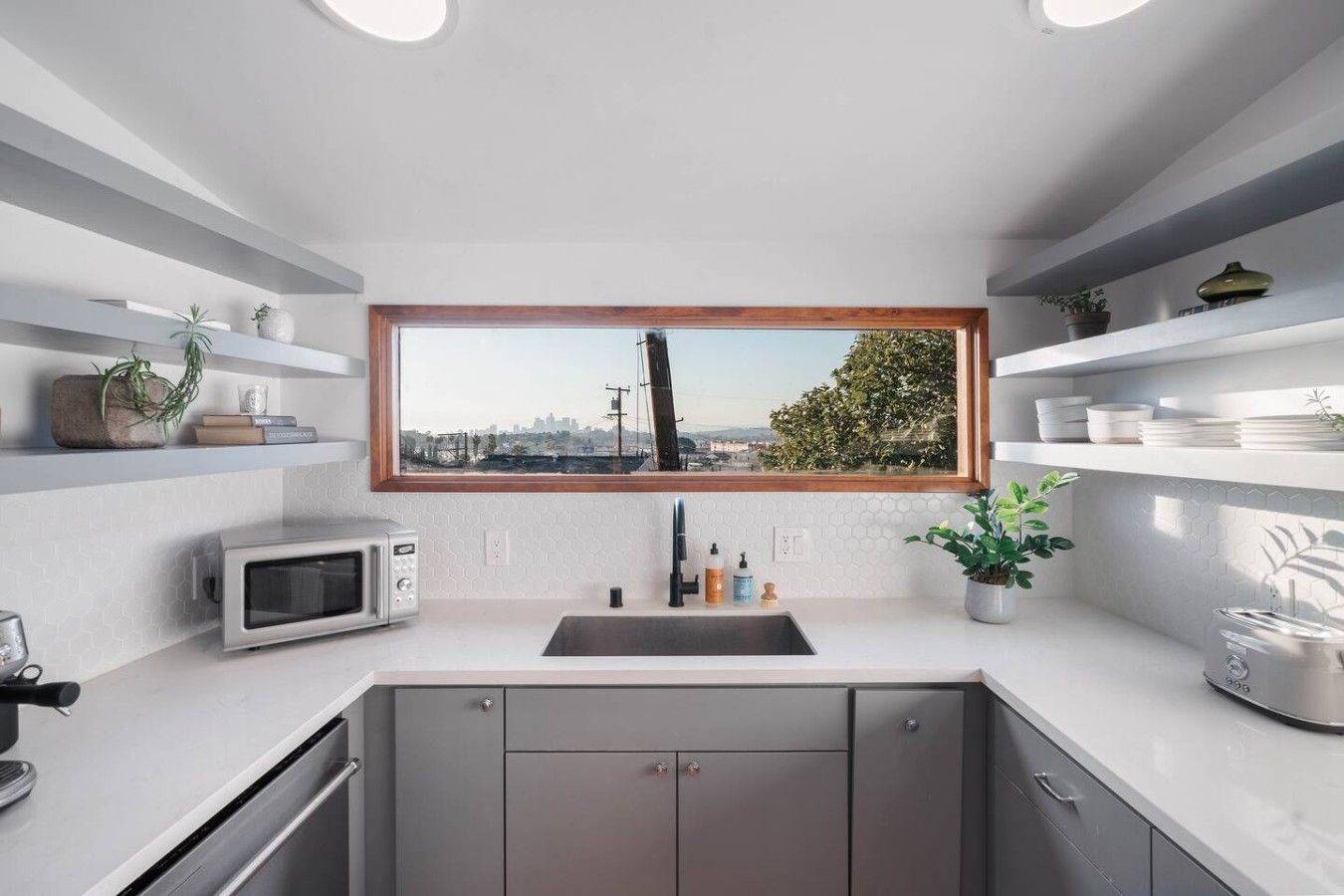 Eine moderne Küche mit Blick auf eine Stadtlandschaft durch ein großes Fenster, einer Mikrowelle, einem Spülbecken und Schränken.