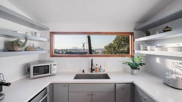 Eine moderne Küche mit Blick auf eine Stadtlandschaft durch ein großes Fenster, einer Mikrowelle, einem Spülbecken und Schränken.