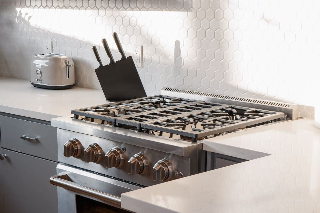 Una cucina con piano cottura in acciaio inossidabile, tostapane e schienale decorato con un motivo esagonale.