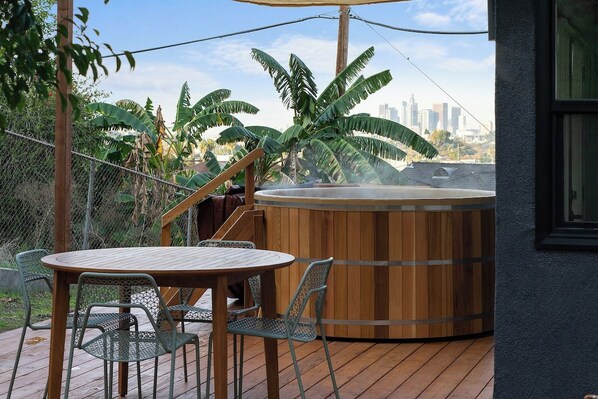 A wooden deck with a hot tub, metal chairs, and a view of a city skyline.