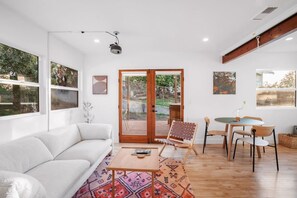 Ein modernes Wohnzimmer mit einer Couch, einem Couchtisch, einem gemusterten Teppich, einem Essbereich mit Stühlen und einer Glastür, die zu einem Außenbereich führt.