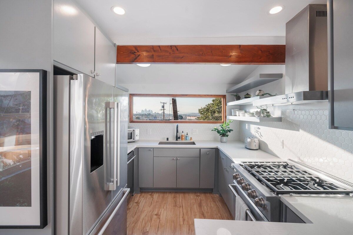 A modern kitchen with a stainless steel refrigerator, a built-in oven, a gas stove, and a window providing a view of the city.