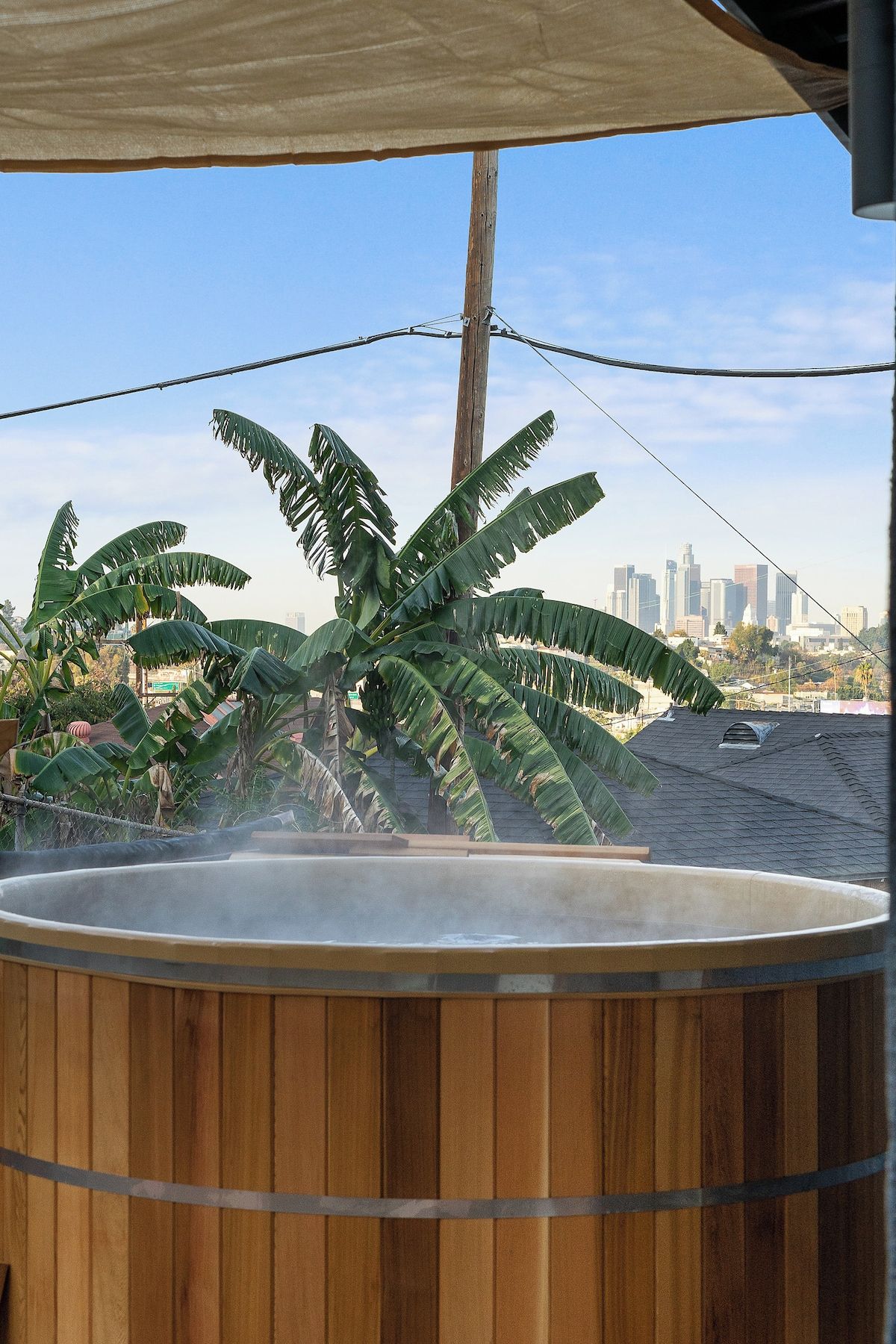 Ein Whirlpool mit Holzverkleidung, umgeben von großen Bananenblättern, mit einer Stadtansicht im Hintergrund.