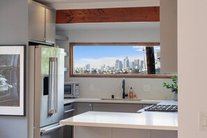 A modern kitchen with a built-in microwave, a stainless steel refrigerator, and a window with a city skyline view.