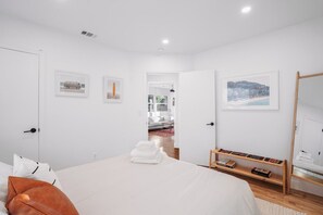 Een moderne slaapkamer met een bed, een nachtkastje met boeken, een spiegel en ingekaderde foto’s aan de muur.