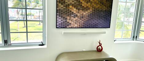 A modern living room with a large wall-mounted TV, a unique curved bench, and large windows with a view of palm trees.