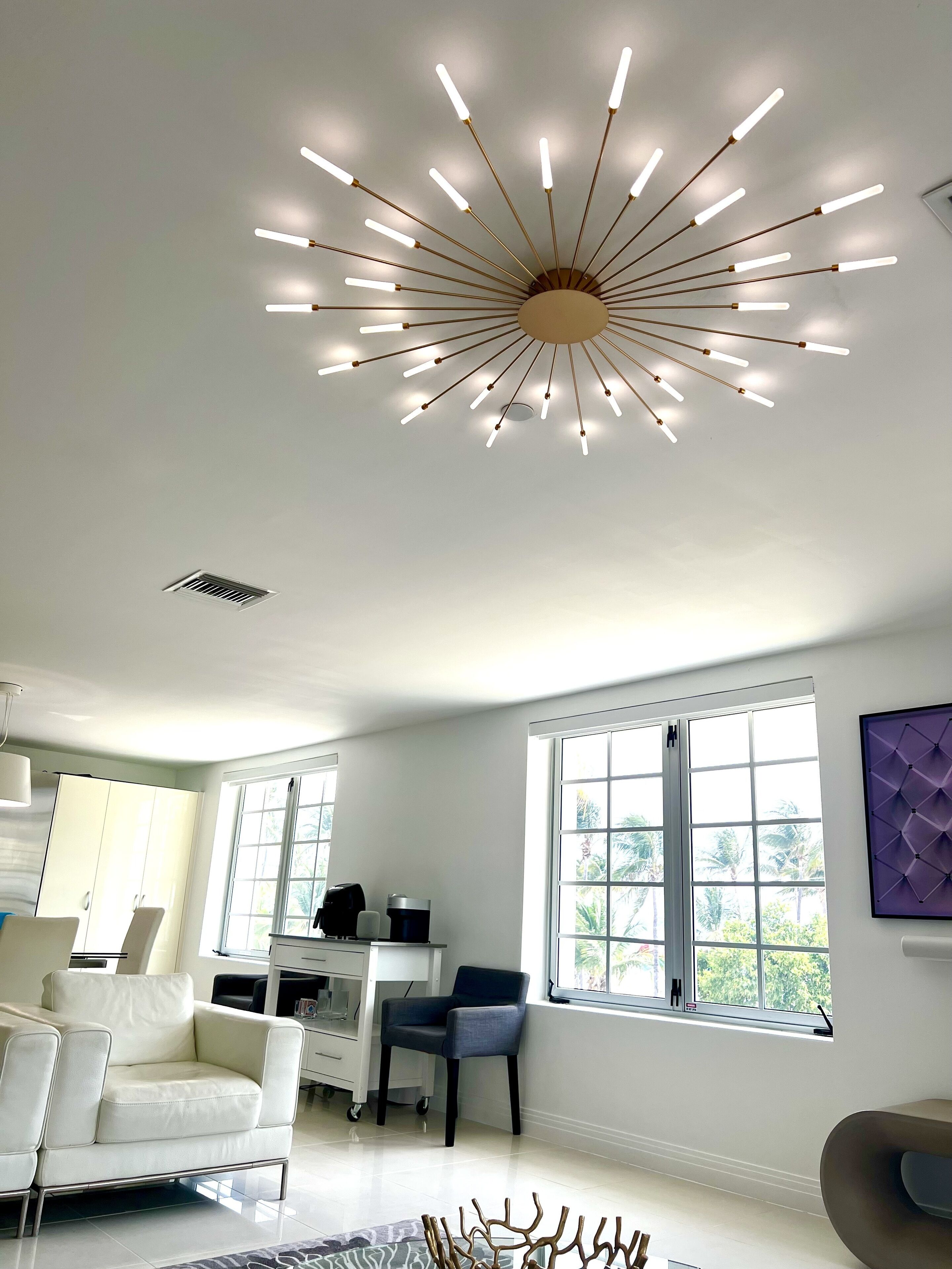 A modern living room with a unique ceiling light fixture, large windows, and contemporary furniture.