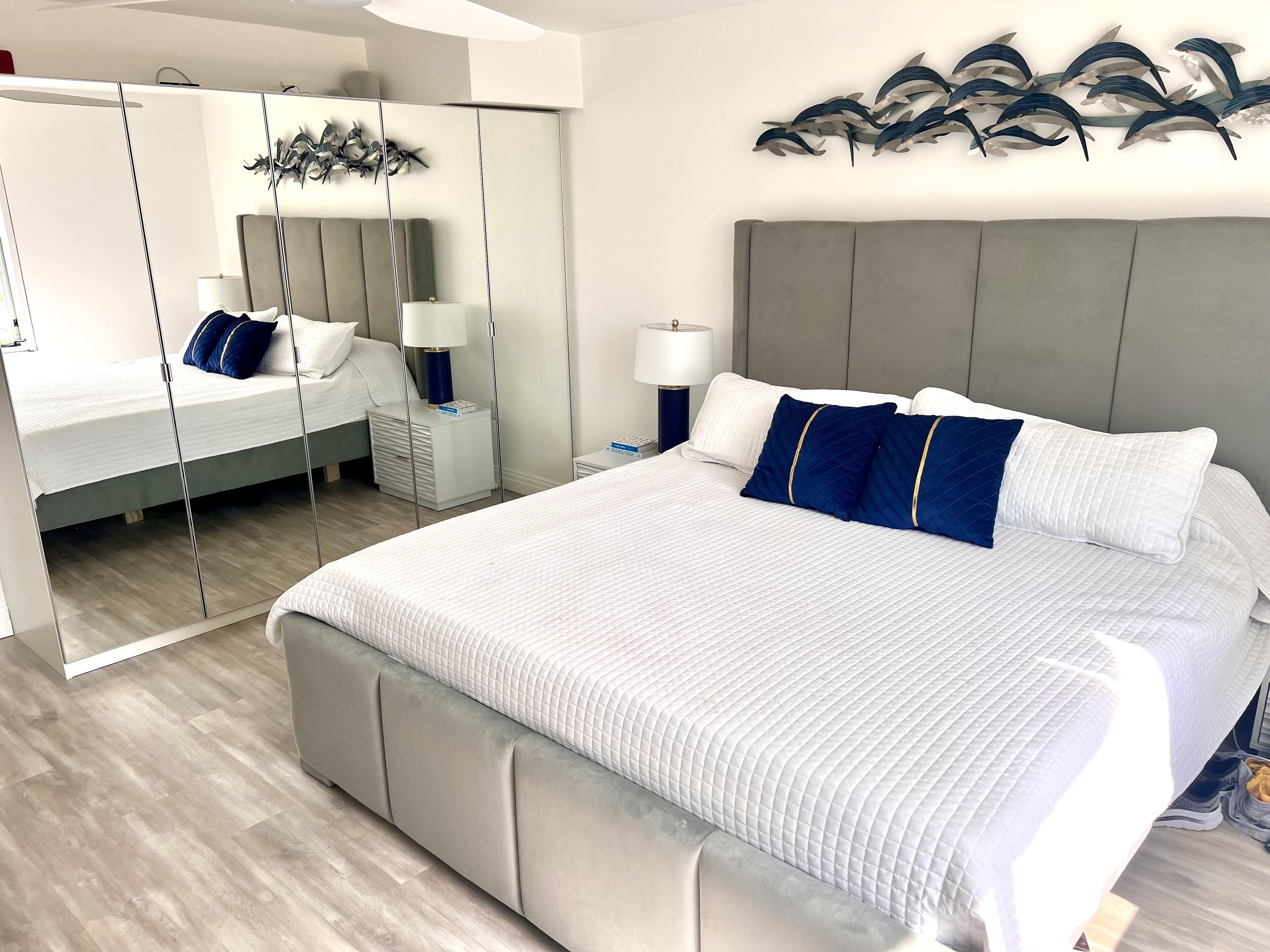 Quarto de hotel moderno com uma cama grande, um guarda-roupa com espelho, uma mesa de cabeceira e uma obra de arte na parede.