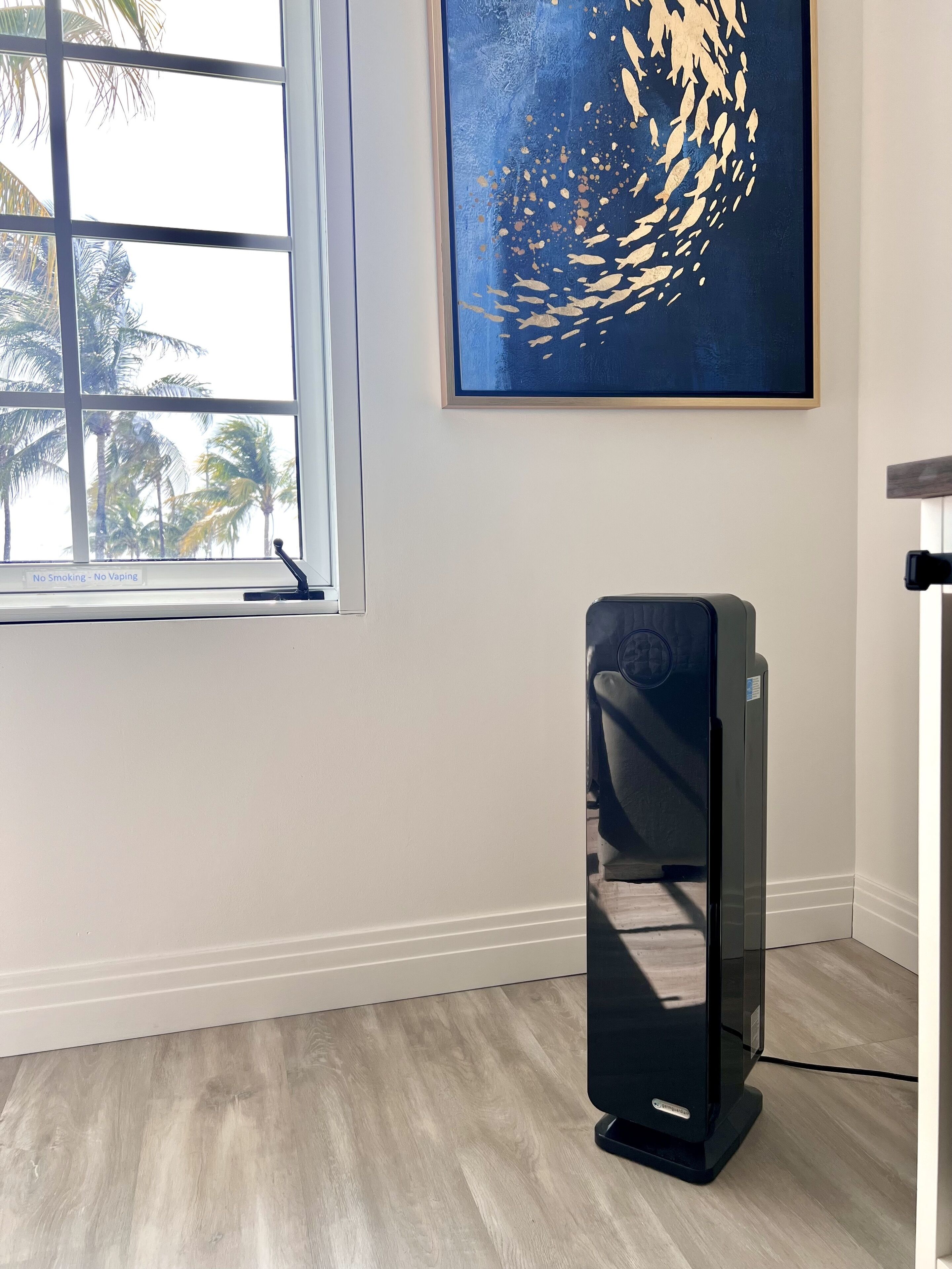 A room with a large window, a wall-mounted artwork, and a standing heater.
