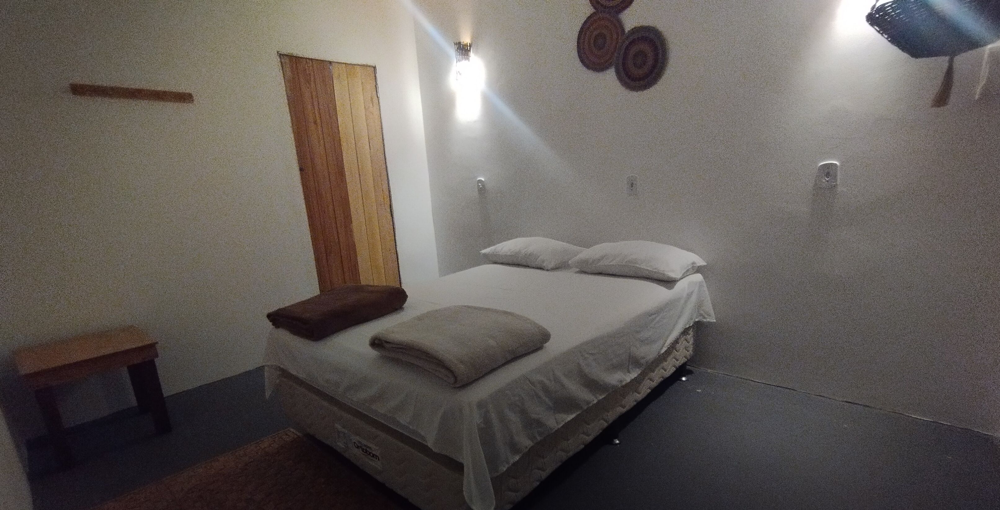 Un dormitorio con cama, mesita de noche, pared de paneles de madera y lámpara de pared.