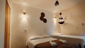Habitación de hotel con dos camas, una puerta de madera, luces fijadas a la pared y un colgador de techo.