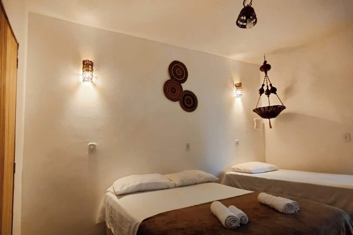 A hotel room with two beds, a wooden door, wall-mounted lights, and a hanging light fixture.
