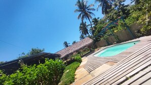 Una terraza de madera con piscina, rodeada de exuberante vegetación y palmeras.