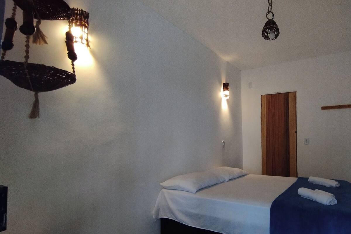 A small, simple room with a bed, a hanging light fixture, and a wooden door.