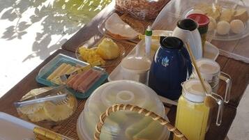 Desayuno con diferentes alimentos y bebidas sobre una mesa al aire libre, cerca de una piscina.